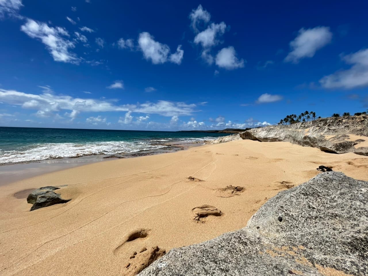 Golden sand and turquoise surf at Kepuhi Beach, with pale rock outcrops and palms along the bluff