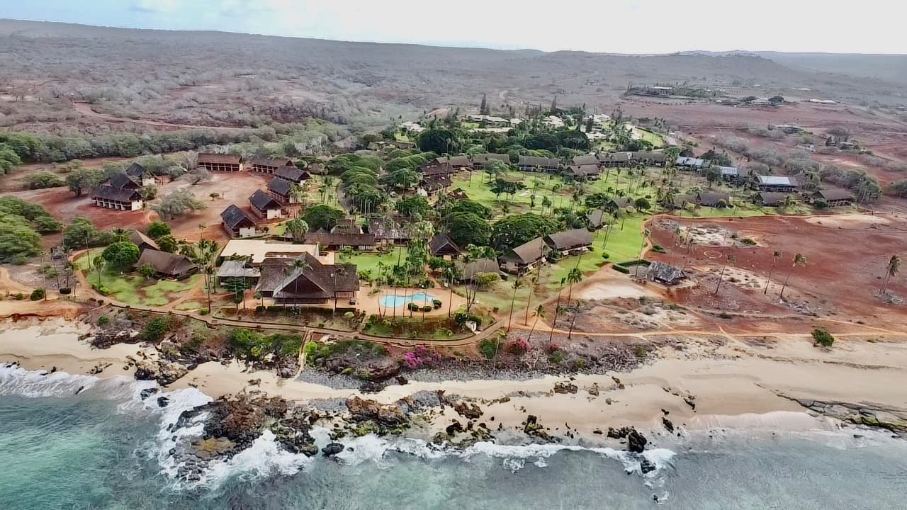 Aerial view of the low-rise resort buildings set among lawns and palms directly above the Kepuhi shoreline